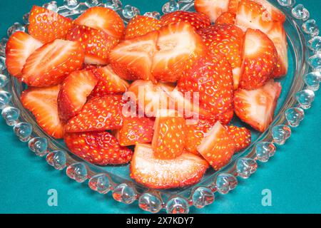 Des pois de fraises dans un bol en forme de coeur sur un fond bleu. Banque D'Images