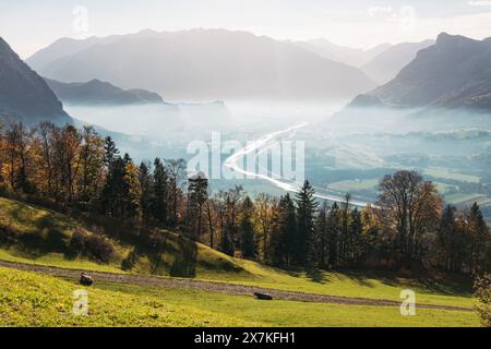 Le Rhin serpente à travers une vallée entourée de montagnes, avec du brouillard persistant dans l'air et des arbres aux couleurs automnales Banque D'Images