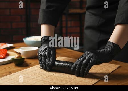 Chef en gants faisant rouler des sushis à la table en bois, gros plan Banque D'Images