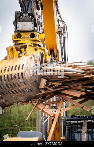 Excavatrice avec grand grappin métallique écrasant un tas de bois et se déplaçant sur un chantier de construction, démolition, Saarbruecken, Allemagne Banque D'Images