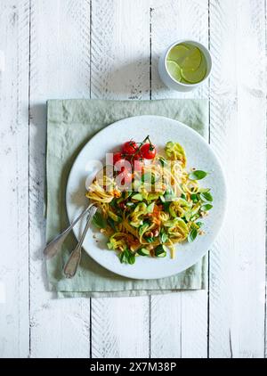 Fleurs de courgettes frites, tomates cerises frites, basilic et noisettes hachées servies avec des spaghettis sur fond blanc en bois Banque D'Images