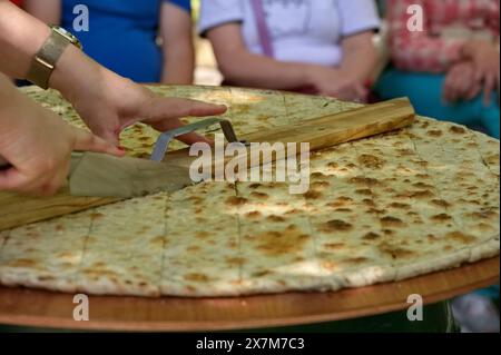 Womans Hands Cut soparnik - cuisine croate traditionnelle sur une grande assiette en bois Banque D'Images