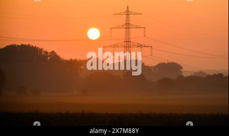 Algermissen, Allemagne. 21 mai 2024. Le soleil se lève derrière une ligne électrique à haute tension dans le quartier de Hildesheim. En 2022, les consommateurs ont soudainement dû creuser profondément dans leurs poches pour obtenir de l'électricité - cela ne devrait plus se produire aussi rapidement dans l'UE. Le feu vert définitif vient d'être donné pour la réforme prévue du marché de l'électricité. Crédit : Julian Stratenschulte/dpa/Alamy Live News Banque D'Images