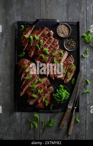 Bifteck de flanc de bœuf sur un plateau de gril noir, raffiné avec du sel fumé et des pointes de pousses d'épinette fraîche Banque D'Images