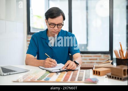 Un designer d'intérieur masculin asiatique expérimenté et professionnel ou un entrepreneur se concentre sur le travail dans son bureau, l'examen du plan de construction, chec Banque D'Images