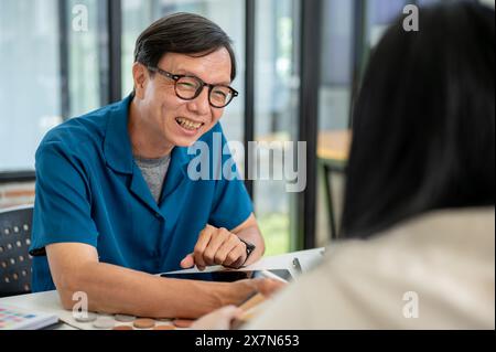Un designer d'intérieur masculin asiatique senior positif, expert ou entrepreneur a une réunion avec une cliente dans le bureau, discutant de la maison inter Banque D'Images