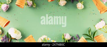 Plat-lay de cônes de gaufre et de fleurs sur fond vert pastel, vue de dessus, plat-lay. Concept d'ambiance printemps ou d'été, bannière, espace de copie Banque D'Images