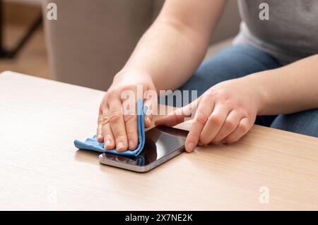 Photo rognée d'une femme méconnue qui nettoie son appareil ou l'écran de son téléphone à la maison Banque D'Images
