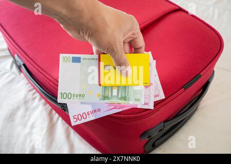 Homme d'affaires méconnaissable montrant des euros et une carte de crédit jaune sur une valise rouge sur un lit Banque D'Images