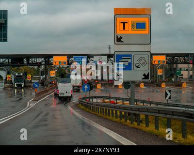 Piacenza, Italie -22 avril 2024 approche d'un poste de péage sur une chaussée mouillée par temps de pluie, avec divers panneaux et une camionnette en vue, jour de pluie sur Motorw Banque D'Images