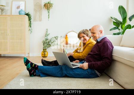 Couple senior ayant un appel vidéo sur un ordinateur portable, souriant à l'écran. Couple senior dans un salon, se connectant avec des proches en ligne. Banque D'Images