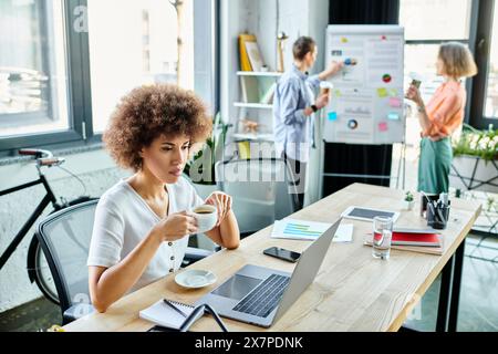 Une femme assise à une table, concentrée sur son ordinateur portable, à côté de ses collègues. Banque D'Images