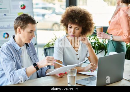Diverses femmes d'affaires s'assoient ensemble à une table, se concentrant sur la paperasserie et discutant des affaires. Banque D'Images
