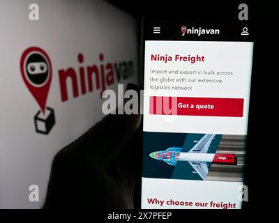 Personne tenant le téléphone portable avec le site Web de la société de livraison singapourienne Ninja Logistics Pte. Ltd. avec logo. Concentrez-vous sur le centre de l'écran du téléphone. Banque D'Images