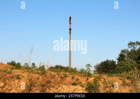 Poteau de ligne électrique en béton avec plusieurs isolateurs en céramique connectant et maintenant des fils électriques allant dans deux directions sur le dessus Banque D'Images