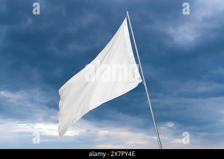 Un drapeau blanc ondule dans le vent avec des nuages sombres en arrière-plan, parfait pour l'état ou la maquette de drapeau publicitaire avec une texture propre Banque D'Images