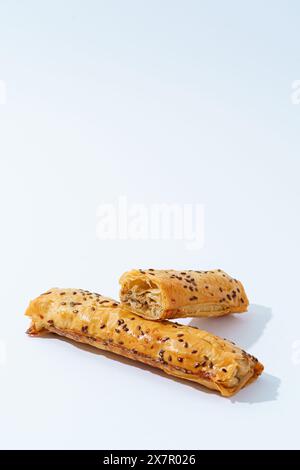 Deux morceaux de pâte feuilletée de veau brun doré recouverts de graines de lin, fraîchement cuits et sertis sur un fond blanc. Banque D'Images