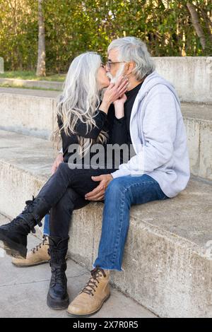 Un couple de personnes âgées profite d'un moment tendre, partageant un baiser assis à l'extérieur sur un pas concret, démontrant un amour durable et la compagnie dans thei Banque D'Images