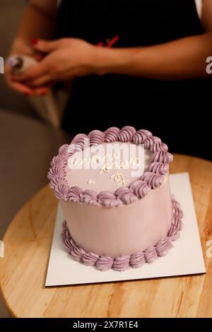 Une personne dans une tenue noire décore un gâteau avec un glaçage violet, mettant en valeur l'art de la pâtisserie et de la conception de gâteaux Banque D'Images