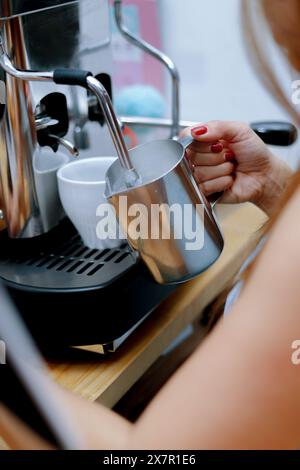 Vue rapprochée d'une main cuisant du lait à la vapeur dans une verseuse métallique à l'aide d'une machine à café professionnelle, idéale pour les recettes de gâteaux Banque D'Images