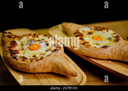 Une vue rapprochée de deux Khachapuris géorgiens traditionnels, chacun rempli de fromage fondu et un œuf parfaitement cuit, affichés esthétiquement sur rustique Banque D'Images