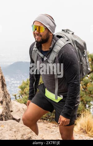 Un randonneur masculin avec un sac à dos s'entraîne sur un sentier de montagne rocheux, portant des lunettes de soleil et des équipements de sport Banque D'Images