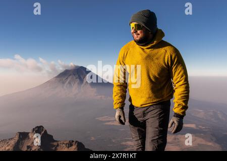 Un randonneur joyeux dans une toison jaune se dresse au sommet d'une crête près du volcan Iztaccihuatl, se prélassant au soleil avec un sourire heureux Banque D'Images