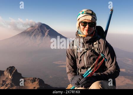 Randonneur souriant dans des poses d'équipement avec le majestueux volcan Iztaccihuatl en toile de fond lors d'une randonnée par jour clair Banque D'Images