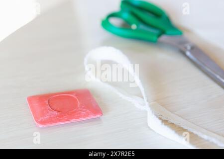 Une image en gros plan montrant des outils de couture, y compris une paire de ciseaux verts, un ruban à mesurer blanc et une craie rose sur une surface en bois, représentant un sewi Banque D'Images