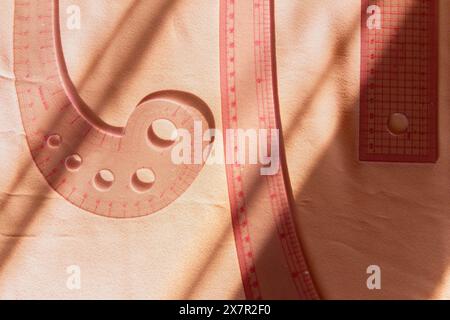 Les outils de confection, y compris une règle courbe et une règle droite, projettent des ombres sur une surface de tissu lisse, incarnant la précision de la conception de vêtements Banque D'Images