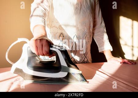 Un individu repasse un morceau de tissu sur une table, baigné de la lumière naturelle du soleil couchant Banque D'Images