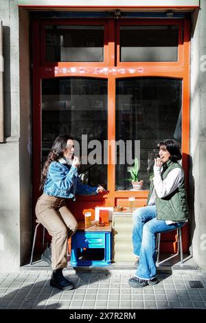 Couple féminin profitant d'une journée ensoleillée ensemble dans un café en plein air, engagé dans une conversation avec des expressions joyeuses. Banque D'Images