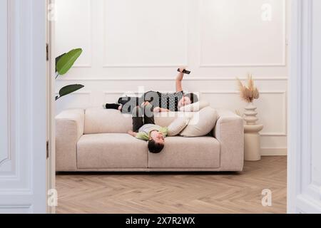 Genre enfant non identifié couché avec les yeux fermés et enfant féminin regardant la télévision, à la fois se détendre sur un canapé confortable à la maison. Banque D'Images