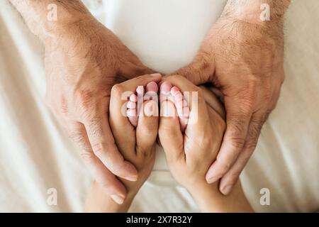 Une image tendre montrant les pieds d'un nouveau-né doucement tenus par les mains aimantes des parents, symbolisant les soins et le lien familial Banque D'Images