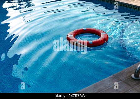 Un anneau rouge vif flotte doucement sur les eaux cristallines d'une piscine sereine, ondulant sous la douce lumière du soleil Banque D'Images