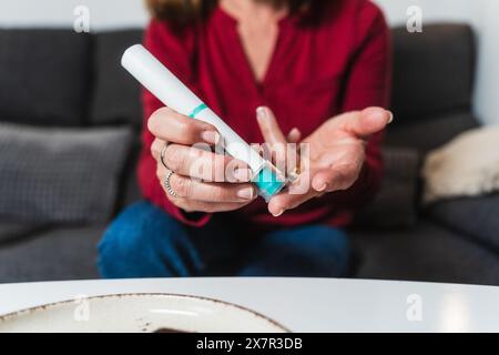Une femme âgée est assise confortablement à la maison alors qu’elle prépare une injection d’insuline, un traitement courant pour gérer l’hypoglycémie chez les diabétiques Banque D'Images