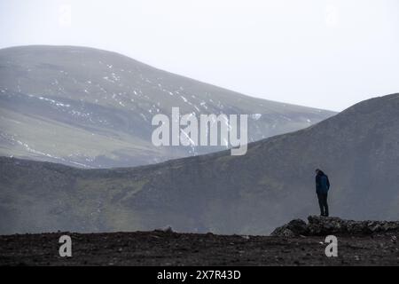 Une figure solitaire se dresse sur un éperon rocheux, contemplant le vaste paysage aride des Highlands islandais enveloppé de brume Banque D'Images