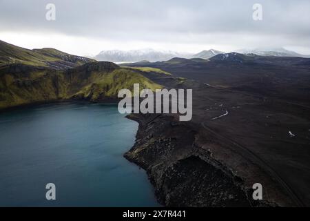 Une photo aérienne capture la beauté sereine d'un lac montagneux flanqué de collines escarpées et d'un vaste terrain volcanique sombre sous un ciel sombre Banque D'Images