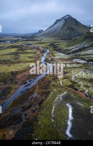 Vue aérienne d'une rivière serpentine serpentant à travers des paysages montagneux parsemés de neige avec une montagne conique en arrière-plan Banque D'Images