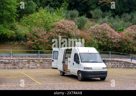 Un fourgon blanc avec portes ouvertes garé sur un parking pavé avec fleurs roses en fleurs et feuillage vert en arrière-plan, indicatif d'un leisu Banque D'Images