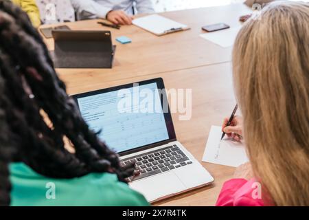 Une équipe diversifiée est engagée dans une session de travail collaboratif dans un espace de coworking, en utilisant un ordinateur portable et en prenant des notes pendant leur réunion Banque D'Images