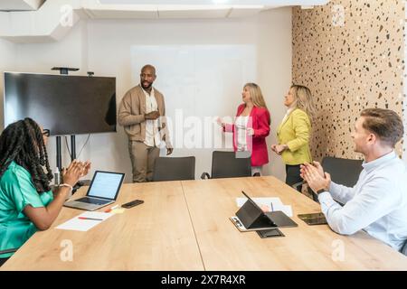 Une équipe de professionnels applaudit un collègue après une présentation réussie dans un espace de bureau de coworking moderne Banque D'Images