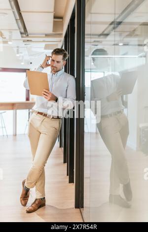 Un professionnel des affaires est capturé marchant et parlant au téléphone tout en tenant un presse-papiers dans un espace de bureau de coworking moderne Banque D'Images