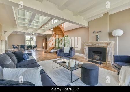 Vaste salon avec un escalier en colimaçon, de grandes poutres et une cheminée classique, meublé avec des canapés modernes et un décor élégant sous le naturel Banque D'Images