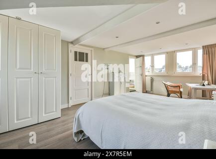 Une chambre bien éclairée et confortable avec un grand lit, des meubles en bois, des armoires blanches et un espace de travail confortable près de la fenêtre Banque D'Images