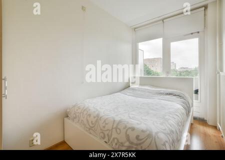 Chambre lumineuse et confortable au design minimaliste, lit simple avec literie à motifs et grande fenêtre baignant de lumière naturelle. Banque D'Images