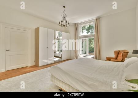 Une chambre spacieuse et bien éclairée avec parquet, un grand lit, un mobilier classique et une abondante lumière naturelle traversant de hautes fenêtres. Banque D'Images