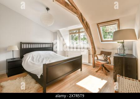 Cette chambre mansardée lumineuse et élégamment meublée comprend des poutres en bois, un grand lit et une fenêtre avec vue. Banque D'Images