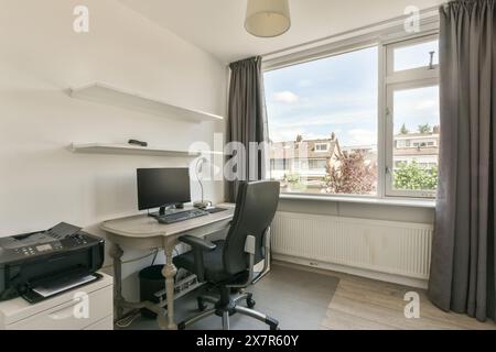 Un bureau à domicile bien organisé avec une configuration de bureau élégant avec ordinateur et imprimante, complétée par des étagères flottantes au-dessus et une grande fenêtre présente Banque D'Images