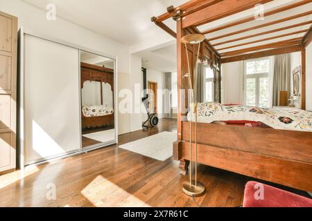 Une chambre spacieuse joliment aménagée avec un grand lit en bois à baldaquin, planchers de bois franc, grande armoire à miroirs, et de hautes fenêtres cette inv Banque D'Images